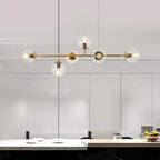 Clear glass orbs, each with a lit bulb, spread along the brass rod of this Clérachic pendant above a stone kitchen counter.