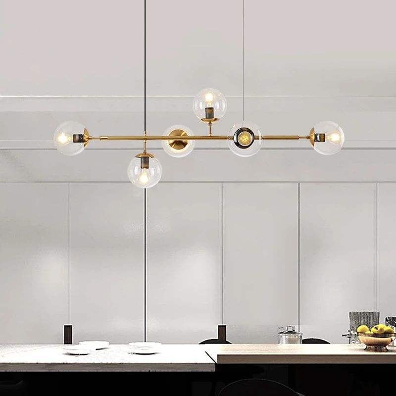 Clear glass orbs, each with a lit bulb, spread along the brass rod of this Clérachic pendant above a stone kitchen counter.
