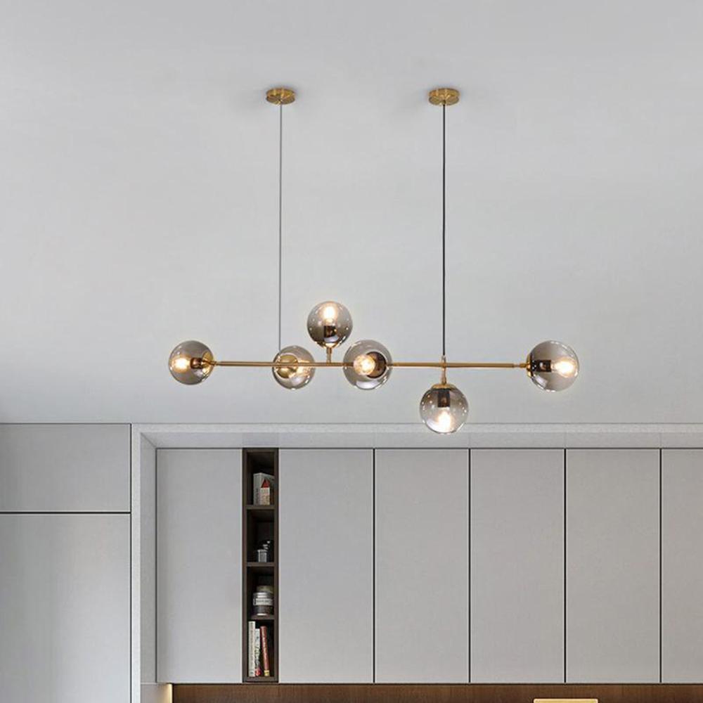Six amber-grey orbs spaced along a brass bar, hung from two ceiling points in front of grey kitchen cabinets, from Clérachic.