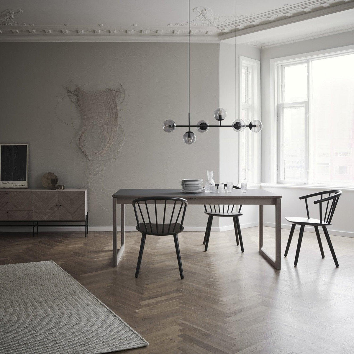 Small in the frame, a black-bar version of this Clérachic pendant with grey glass orbs floats over a dark dining table and spindle chairs.