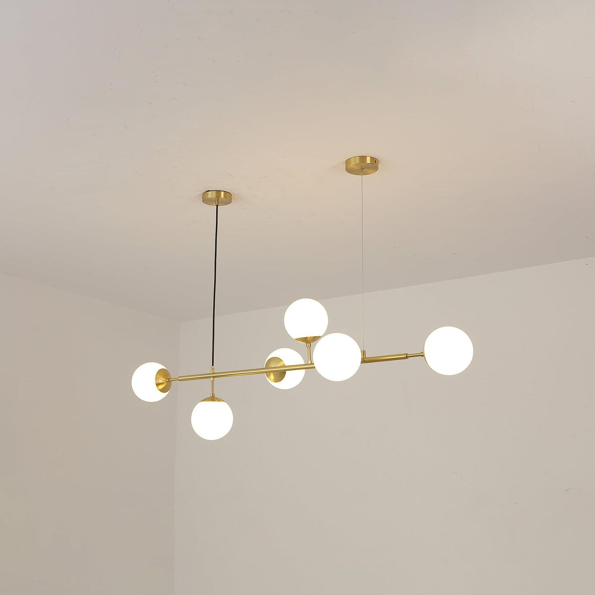 A Clérachic pendant with six frosted white orbs on a brass rod, photographed from below against a cream ceiling corner.