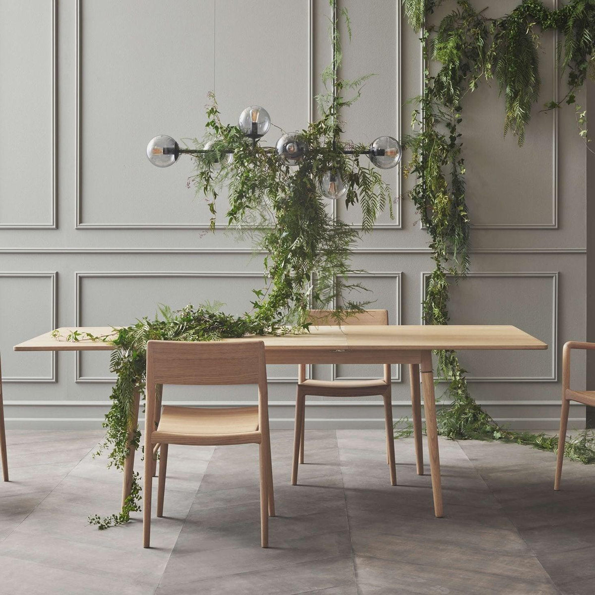 Dark glass orbs on a slim bar hang above a pale oak table swathed in trailing greenery, in this Clérachic pendant.