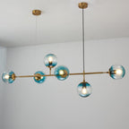 Teal-blue glass orbs, each lit, are strung along the brass rod of this Clérachic pendant against a plain white wall.