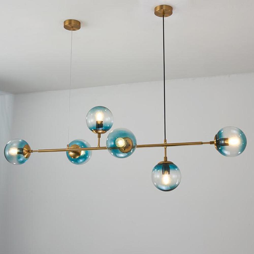 Teal-blue glass orbs, each lit, are strung along the brass rod of this Clérachic pendant against a plain white wall.