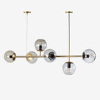 Product shot of this Clérachic pendant on white: six clear glass orbs with visible bulbs along a brass rod and two canopies.