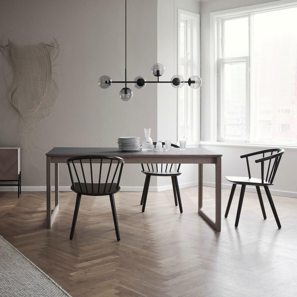 A black-bar version of this Clérachic pendant with smoked orbs hangs in a bright room over a grey table and black spindle chairs.