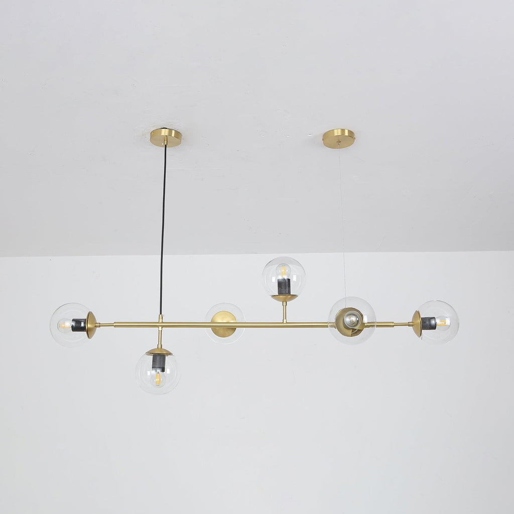 Clear orbs with their bulbs showing, strung along a brass rod from a single black cord, in a Clérachic pendant on a white wall.