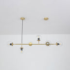 Clear orbs with their bulbs showing, strung along a brass rod from a single black cord, in a Clérachic pendant on a white wall.