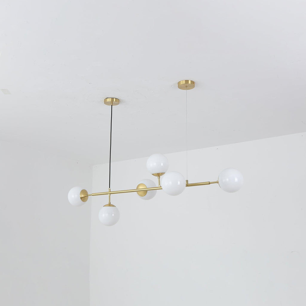 Opal white orbs, switched off, along a slim brass rod in this Clérachic pendant, shown tilted against a plain white room corner.