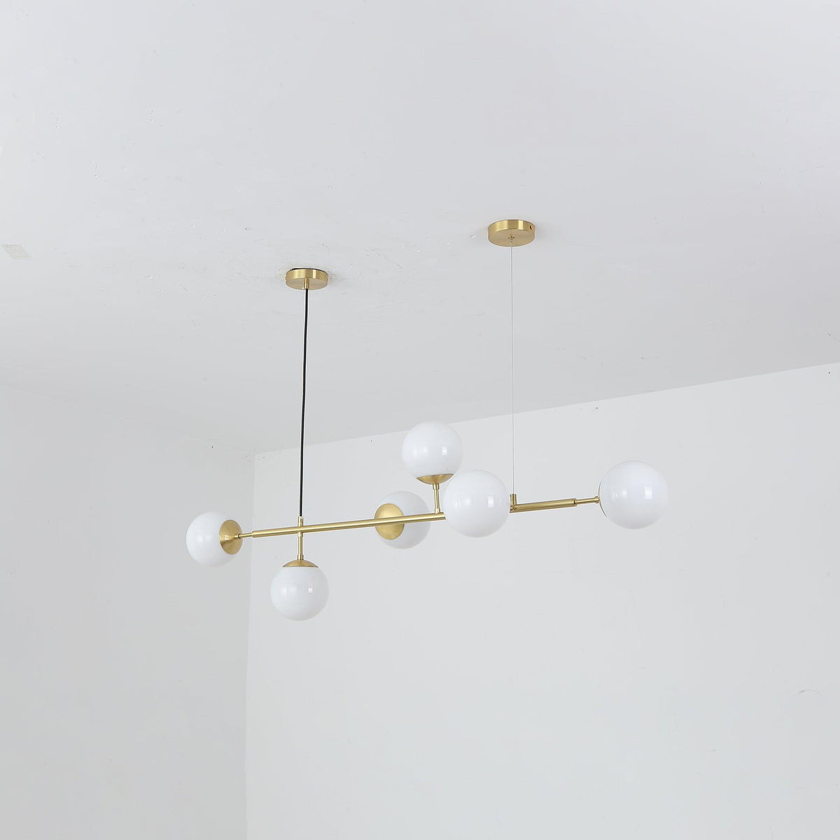Opal white orbs, switched off, along a slim brass rod in this Clérachic pendant, shown tilted against a plain white room corner.