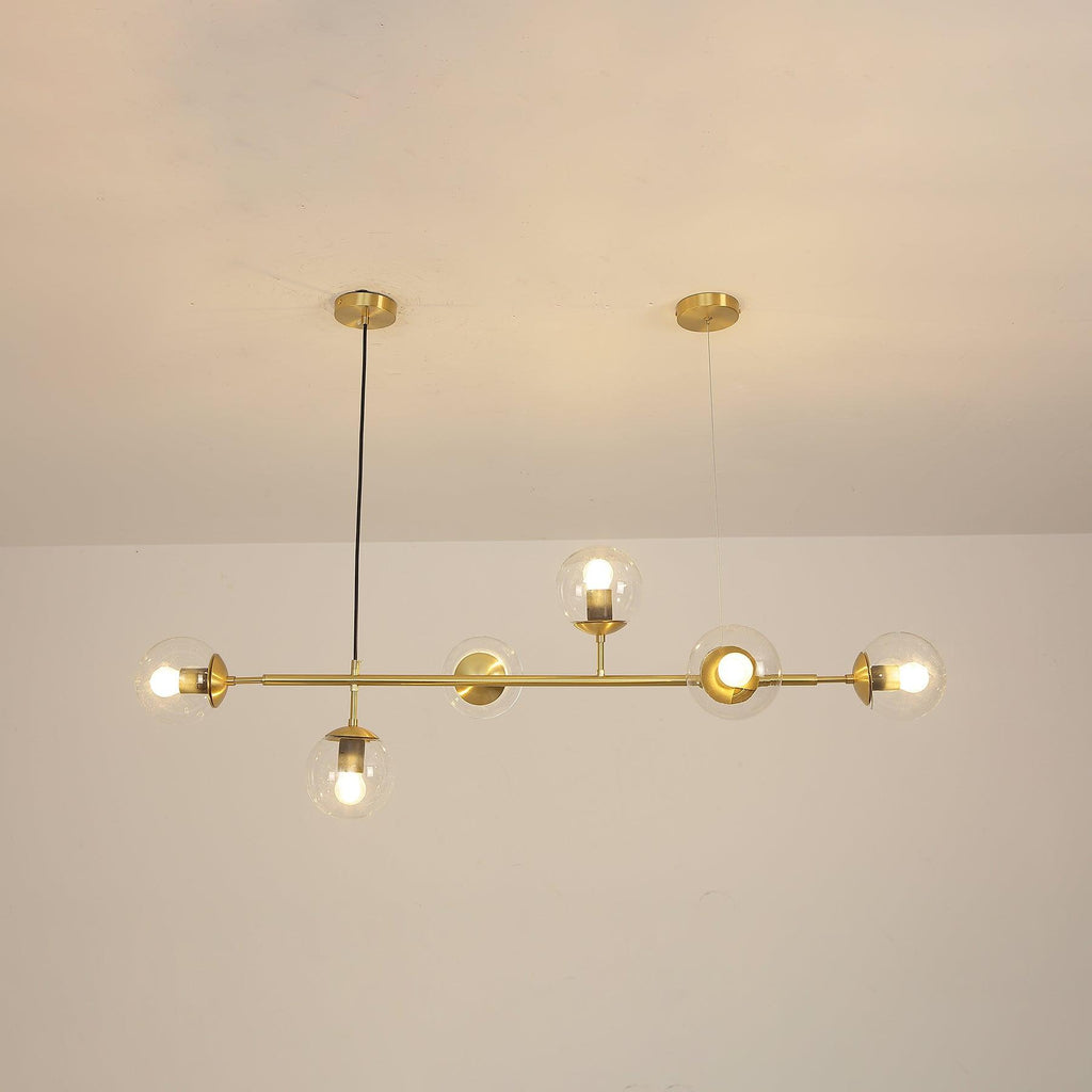 Switched on, the clear orbs of this Clérachic pendant cast a warm amber glow along the brass rod in a cream-toned room.