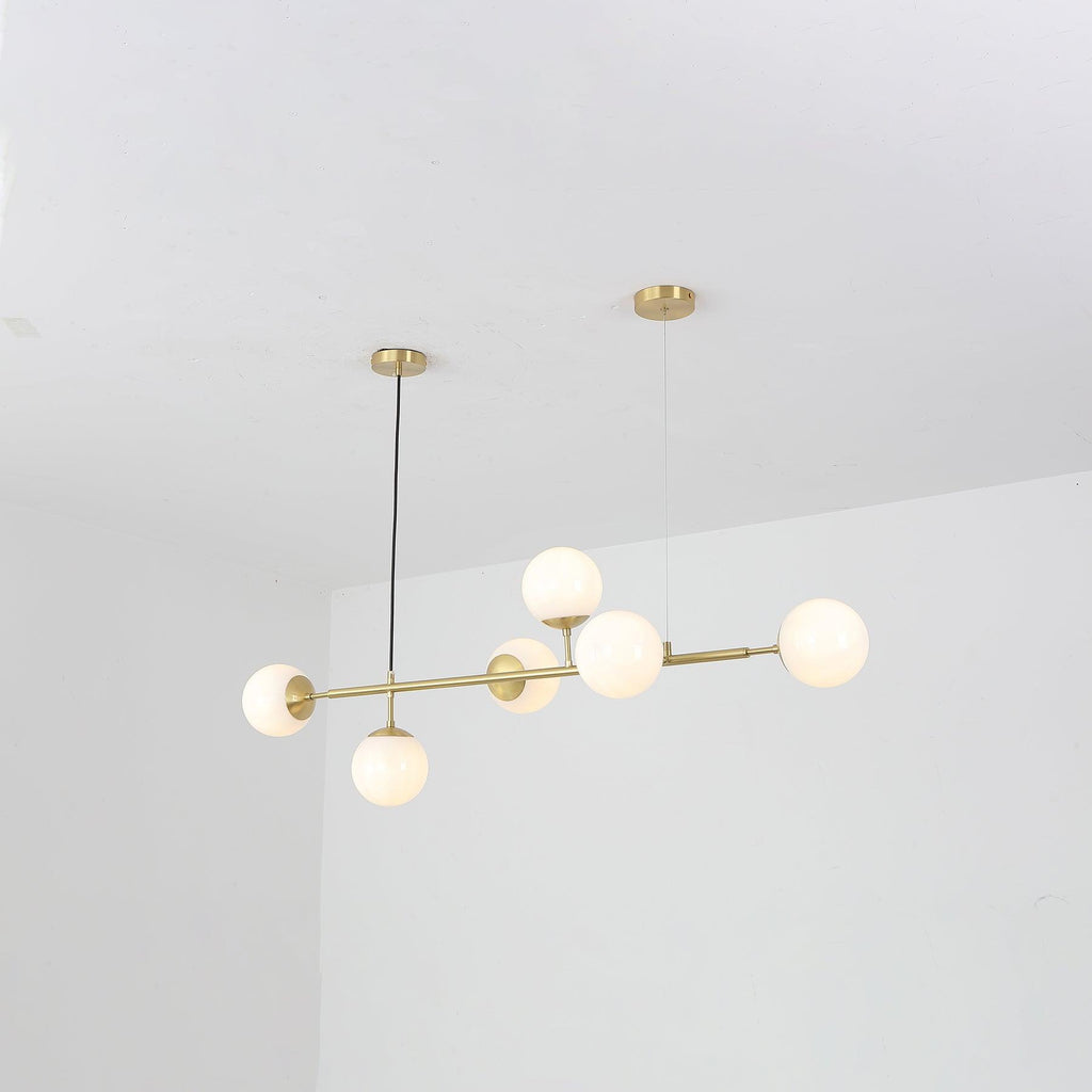 Six opal white orbs glow softly along the brass bar of this Clérachic pendant, seen from a low angle in a white room.