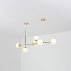Six opal white orbs glow softly along the brass bar of this Clérachic pendant, seen from a low angle in a white room.