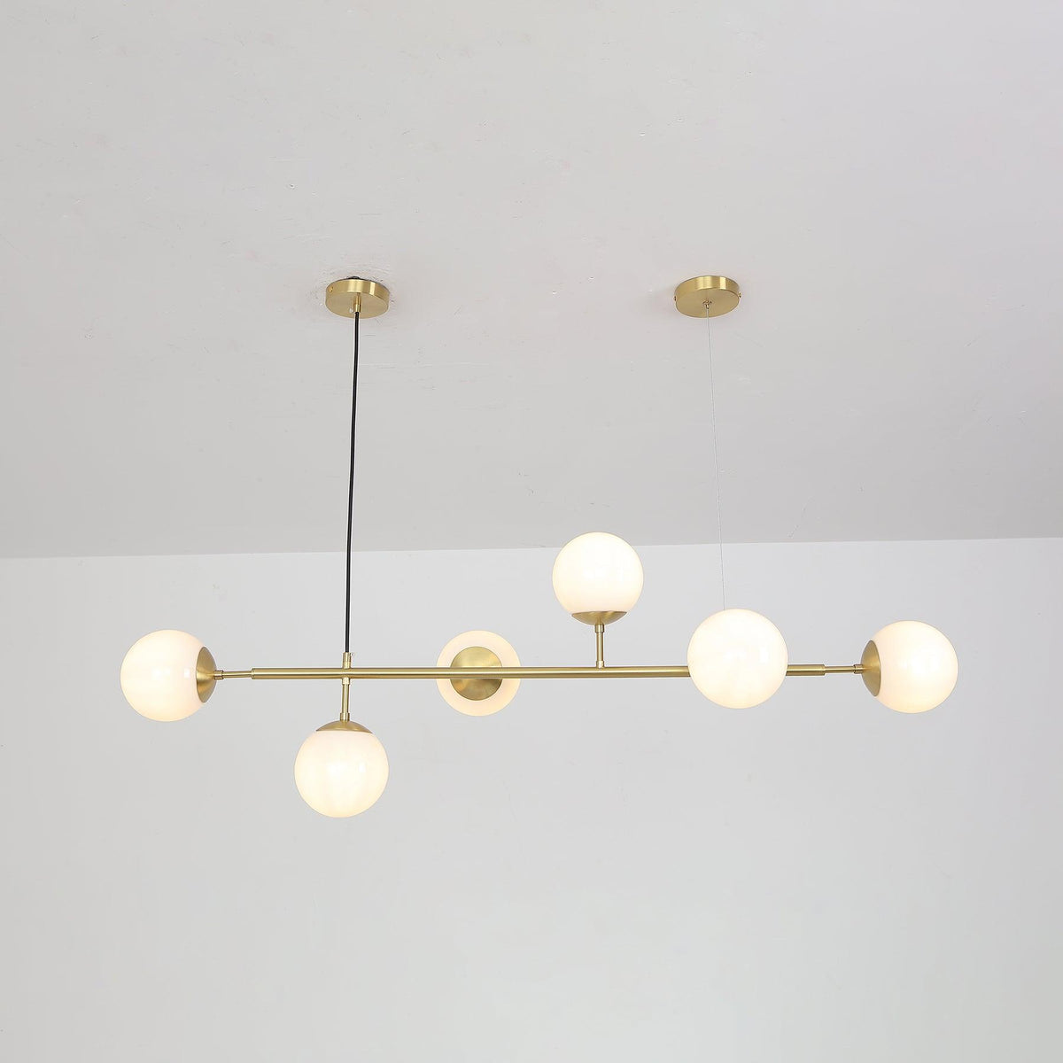 Lit white globes with a soft even glow hang along the brass rod of this Clérachic pendant, below a white ceiling.