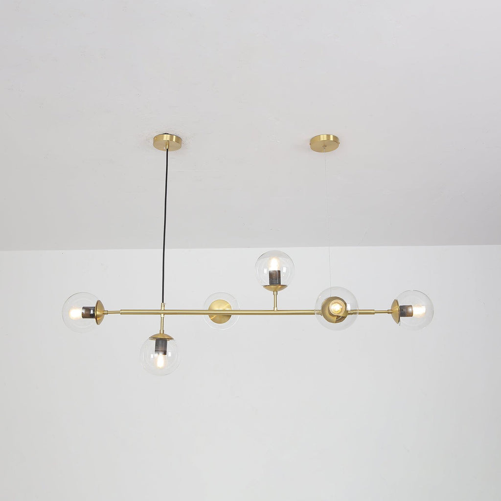Unlit clear glass orbs show their bulb holders along the brass rod of this Clérachic pendant, with a white room behind.