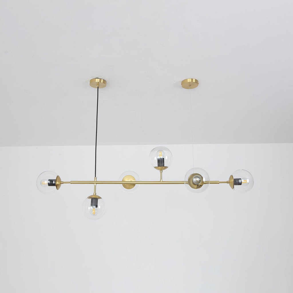 Straight-on view of this Clérachic pendant, its six clear orbs and bulbs hanging evenly from a brass rod below a white ceiling.