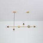 Straight-on view of this Clérachic pendant, its six clear orbs and bulbs hanging evenly from a brass rod below a white ceiling.