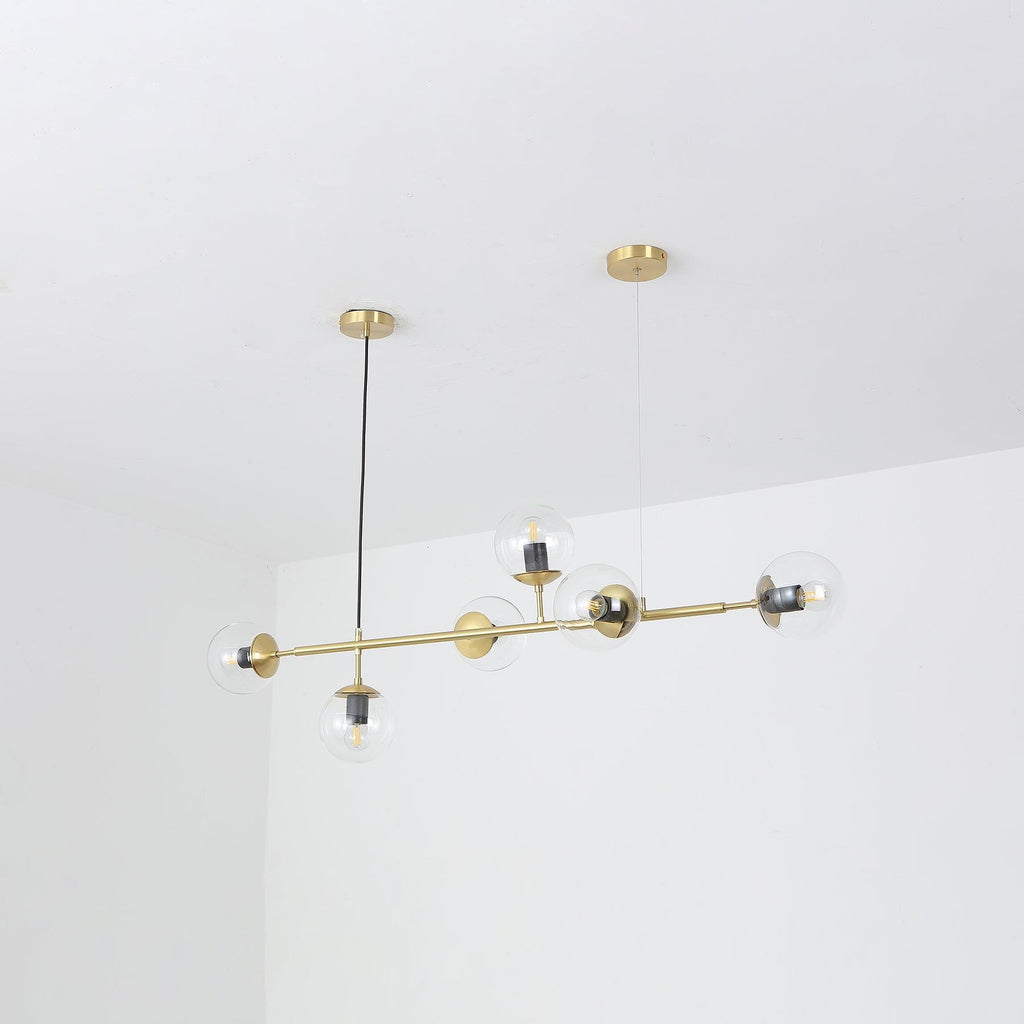 A Clérachic pendant on its brass rod, hung at a slight angle in a white corner, with clear glass orbs and visible bulbs.