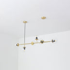 A Clérachic pendant on its brass rod, hung at a slight angle in a white corner, with clear glass orbs and visible bulbs.