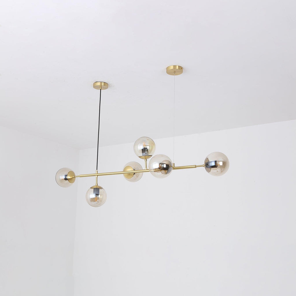 Six amber-tinted glass orbs cluster along the brass rod of this Clérachic pendant, photographed in a white room corner.