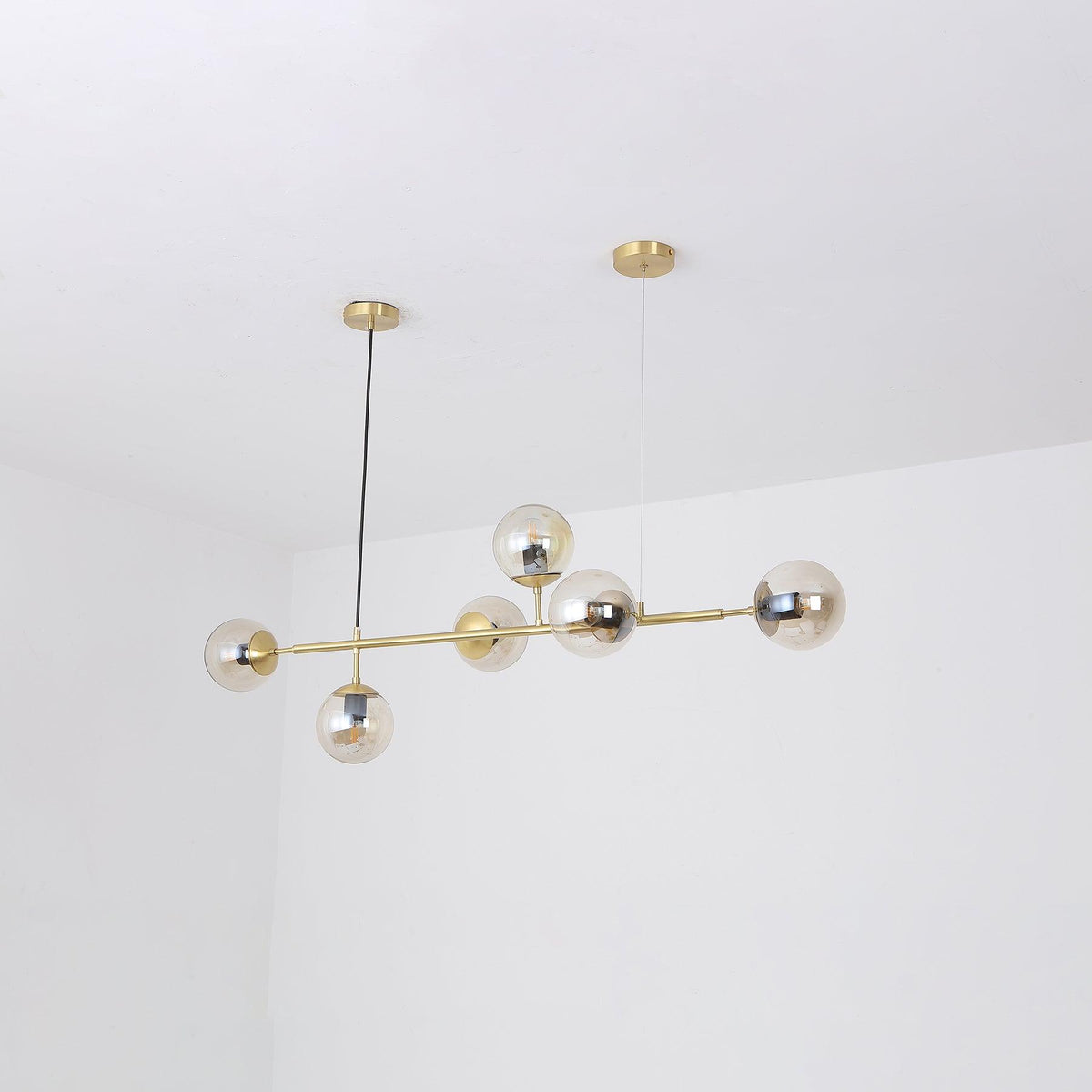 Six amber-tinted glass orbs cluster along the brass rod of this Clérachic pendant, photographed in a white room corner.