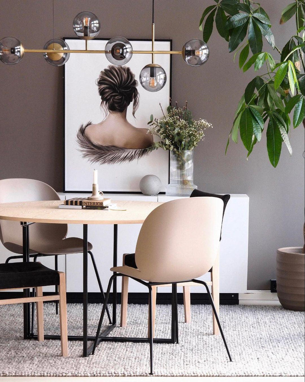 Beside a round table and beige chairs, the brass bar and smoky glass orbs of this Clérachic pendant frame a framed portrait print.