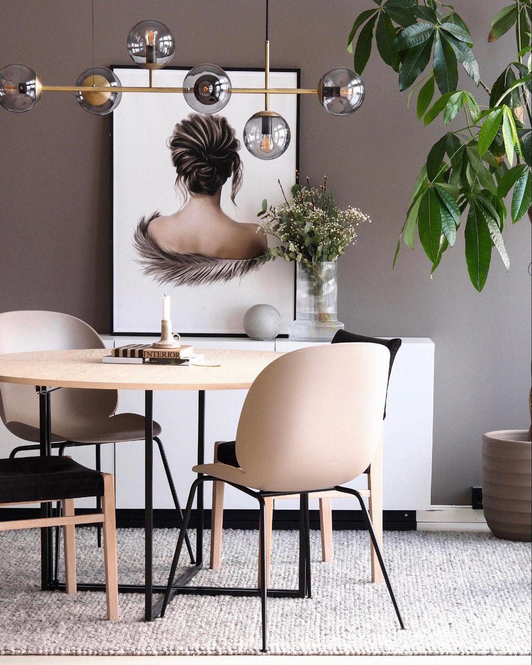 Beside a round table and beige chairs, the brass bar and smoky glass orbs of this Clérachic pendant frame a framed portrait print.