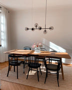 A slim black bar with six smoke-grey orbs hangs in a sunny room over a wood dining table and black bentwood chairs, from Clérachic.