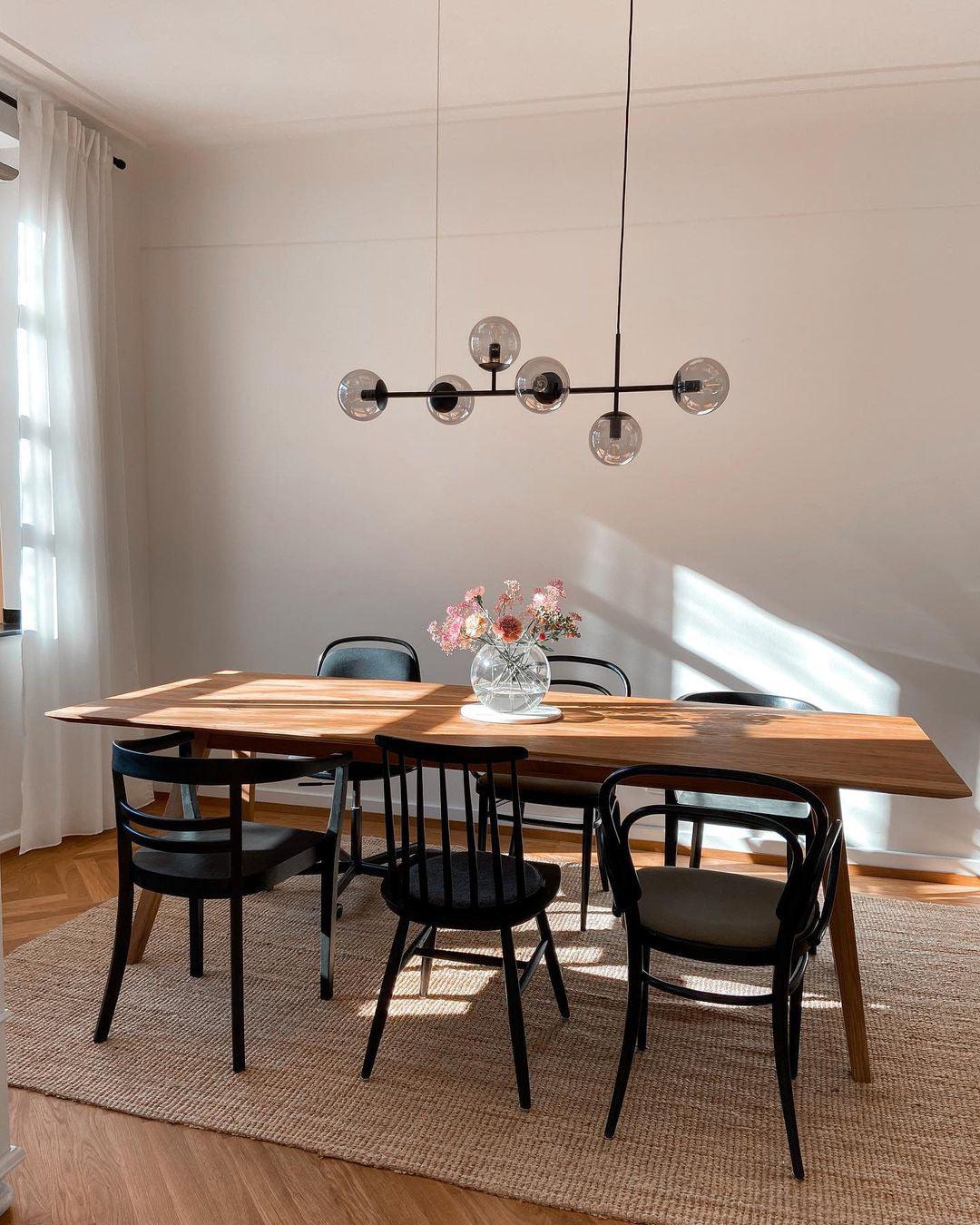 A slim black bar with six smoke-grey orbs hangs in a sunny room over a wood dining table and black bentwood chairs, from Clérachic.