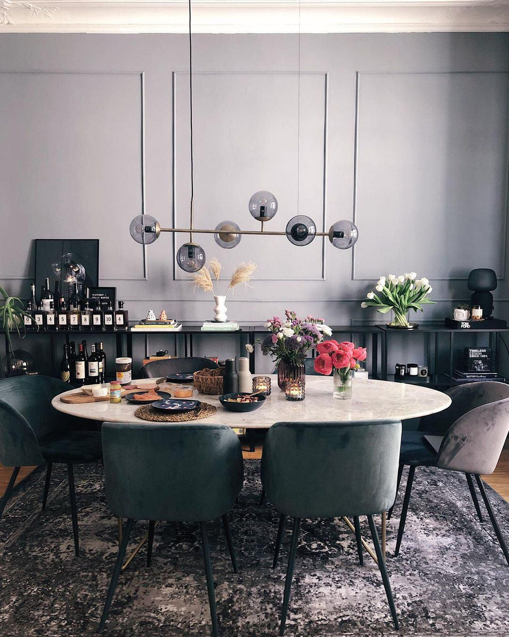 A black-framed row of smoke-grey orbs hangs over an oval marble dining table in a dark grey room, in this Clérachic pendant.