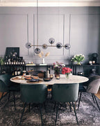 A black-framed row of smoke-grey orbs hangs over an oval marble dining table in a dark grey room, in this Clérachic pendant.