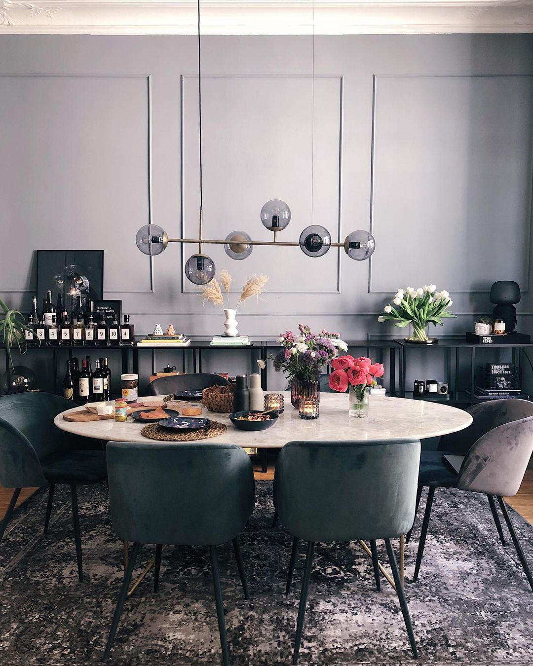 A black-framed row of smoke-grey orbs hangs over an oval marble dining table in a dark grey room, in this Clérachic pendant.