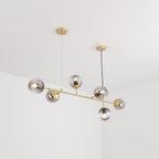 From below, the brass tubing and six smoke-grey orbs of this Clérachic pendant hang from two canopies in a white room.