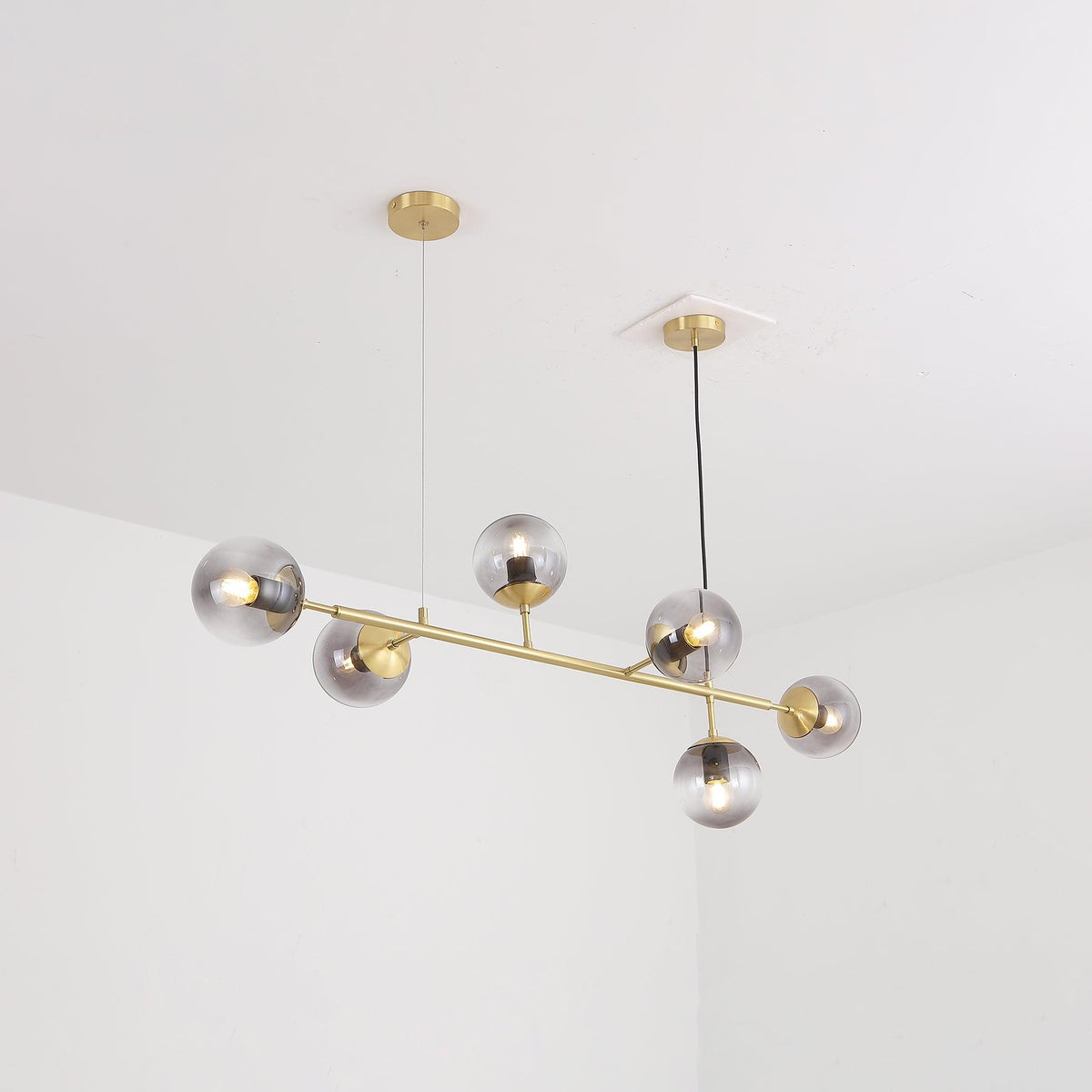 From below, the brass tubing and six smoke-grey orbs of this Clérachic pendant hang from two canopies in a white room.