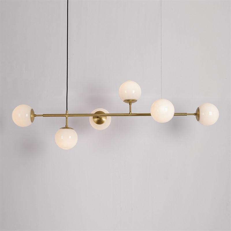 Opal white glass orbs along a brass rod, unlit, on a pale grey backdrop, in this Clérachic pendant with its black cord.
