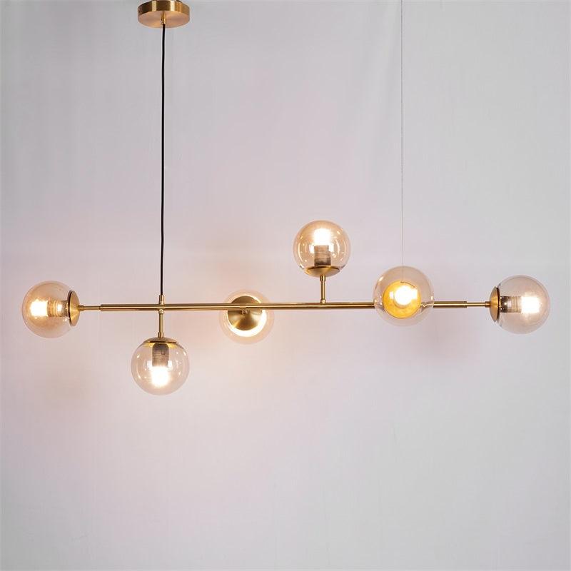 Warm amber light glows from six glass orbs on the brass bar of this Clérachic pendant, shown on a plain grey backdrop.