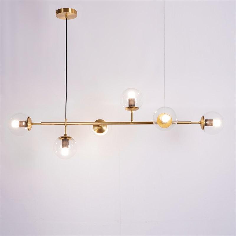 Clear orbs lit from within along a brass bar, with a black cord and brass canopy, in this Clérachic pendant on a lilac-grey backdrop.