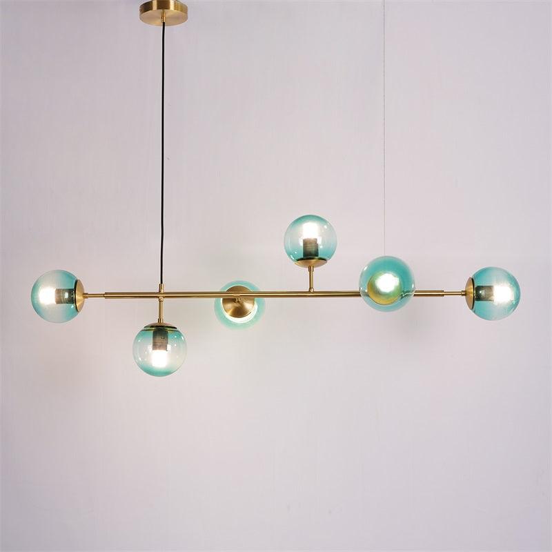 Teal-blue gradient orbs lit warm along a brass bar, from a black cord and brass canopy, on a plain light backdrop, from Clérachic.
