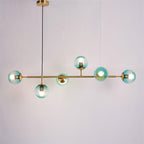 Teal-blue gradient orbs lit warm along a brass bar, from a black cord and brass canopy, on a plain light backdrop, from Clérachic.