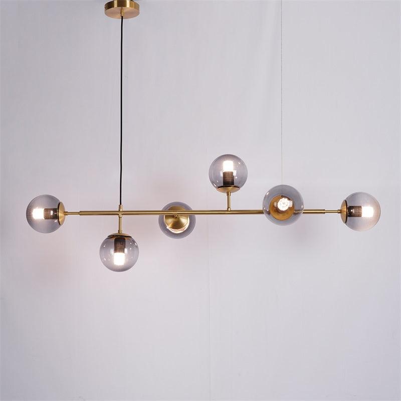 Smoke-grey orbs with a lit bulb in each, along the brass bar of this Clérachic pendant, on a plain pale backdrop.