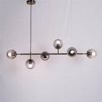 A black-bar Clérachic pendant with smoke-grey orbs, each with a lit bulb, hanging on a black cord against a plain backdrop.