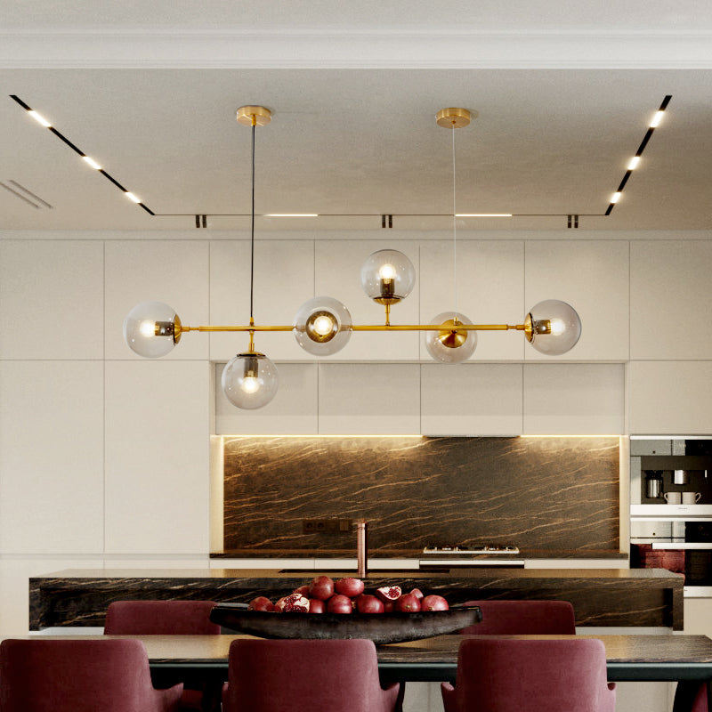 Over a dark marble kitchen island with red stools, the brass bar and clear orbs of this Clérachic pendant glow in warm light.