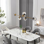 This Clérachic pendant carries smoke-grey orbs on a brass bar above a marble dining table in a bright room with tall windows.