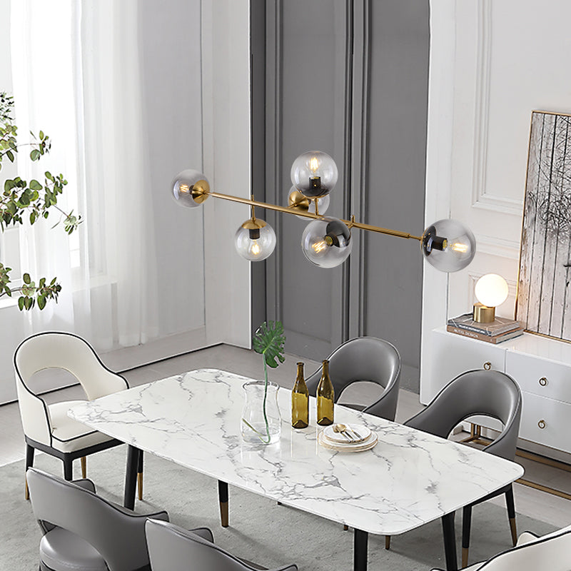 This Clérachic pendant carries smoke-grey orbs on a brass bar above a marble dining table in a bright room with tall windows.