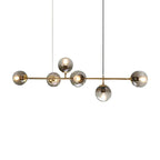 Smoked glass orbs of graduated grey sit on the brass bar of this Clérachic pendant, shown cut out on a white backdrop.