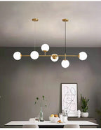 Six opal white orbs lit on a brass rod, hanging in a grey dining room with a framed line print, in this Clérachic pendant.