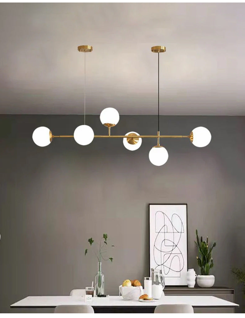 Six opal white orbs lit on a brass rod, hanging in a grey dining room with a framed line print, in this Clérachic pendant.