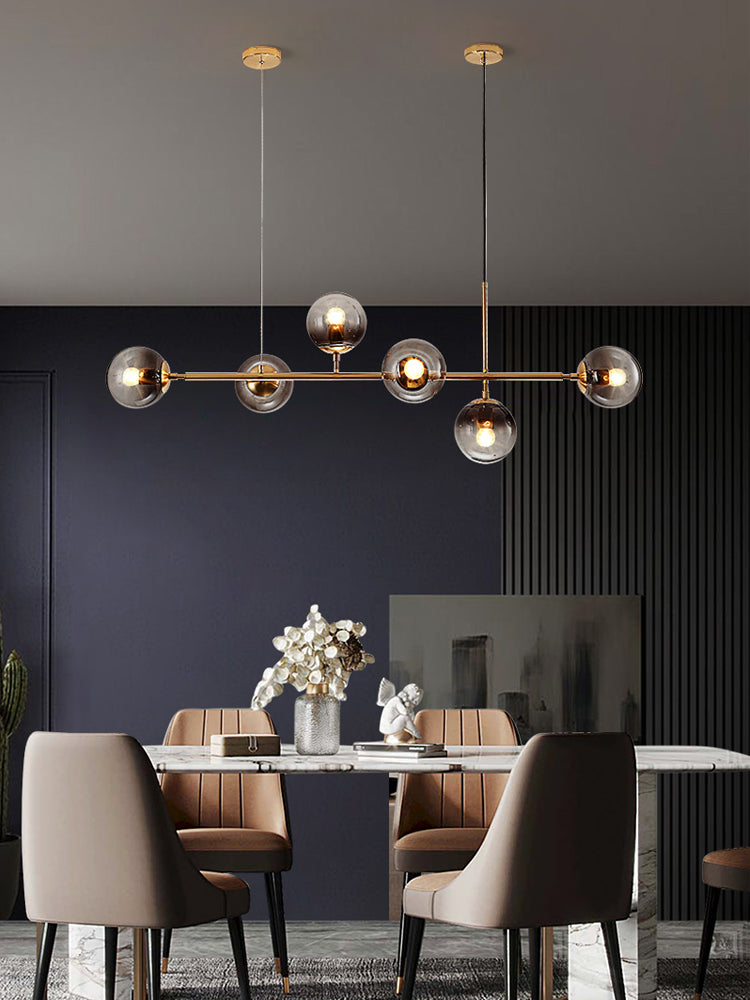 A Clérachic pendant of smoke-grey orbs on a brass rod glows over a marble table before a deep navy panelled wall.