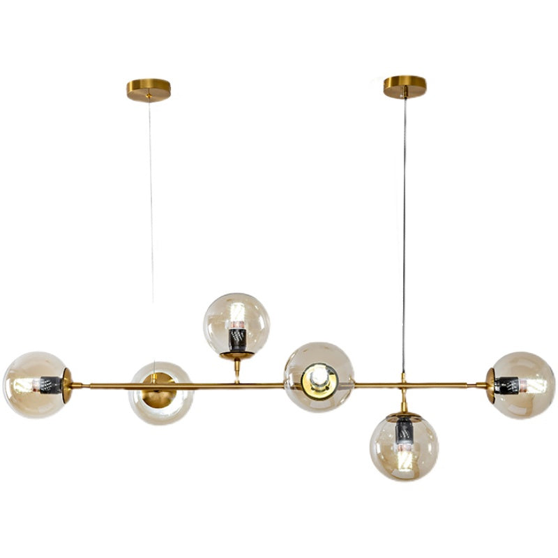 Product shot of this Clérachic pendant on white, with six amber glass orbs and visible bulbs along a brass rod.