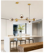 A Clérachic pendant with smoke-grey orbs on a brass rod hangs above a white island and wooden bench in a bright open kitchen.